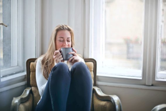Introvertiert: Blonde Frau entspannt auf Sessel am Fenster mit einer Tasse Tee