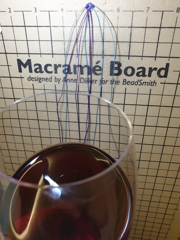 Makramee-Board mit 8 Fäden, im Vordergrund ein Glas Rotwein