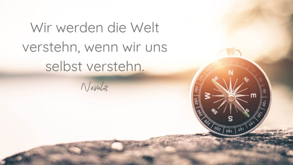 Kompass auf einem Felsen in gold-gelbem Licht mit einem Zitat von Novalis: Wir werden die Welt verstehn, wenn wir uns selbst verstehn.