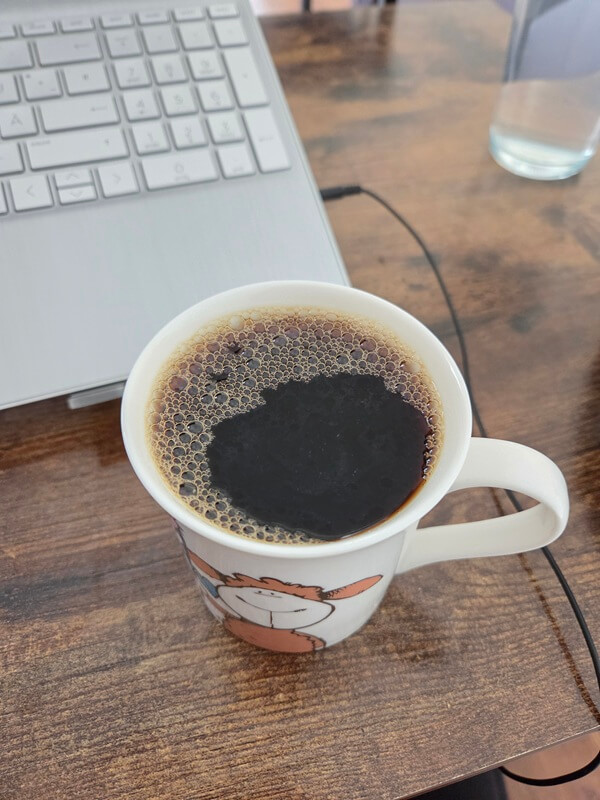 Dampfende Kaffeetasse auf einem Holzschreibtisch neben einem geöffneten Laptop.