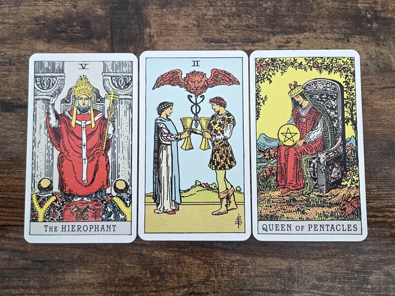 Psychologisches Tarot für empathisches Abgrenzen: 3 Tarotkarten auf einem Holztisch zum Thema „Andere zweifeln unsere Beziehung an. Haben sie recht?“