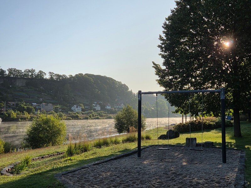 Ein Spielplatz am Elbufer und Flussnebel in der Morgensonne.